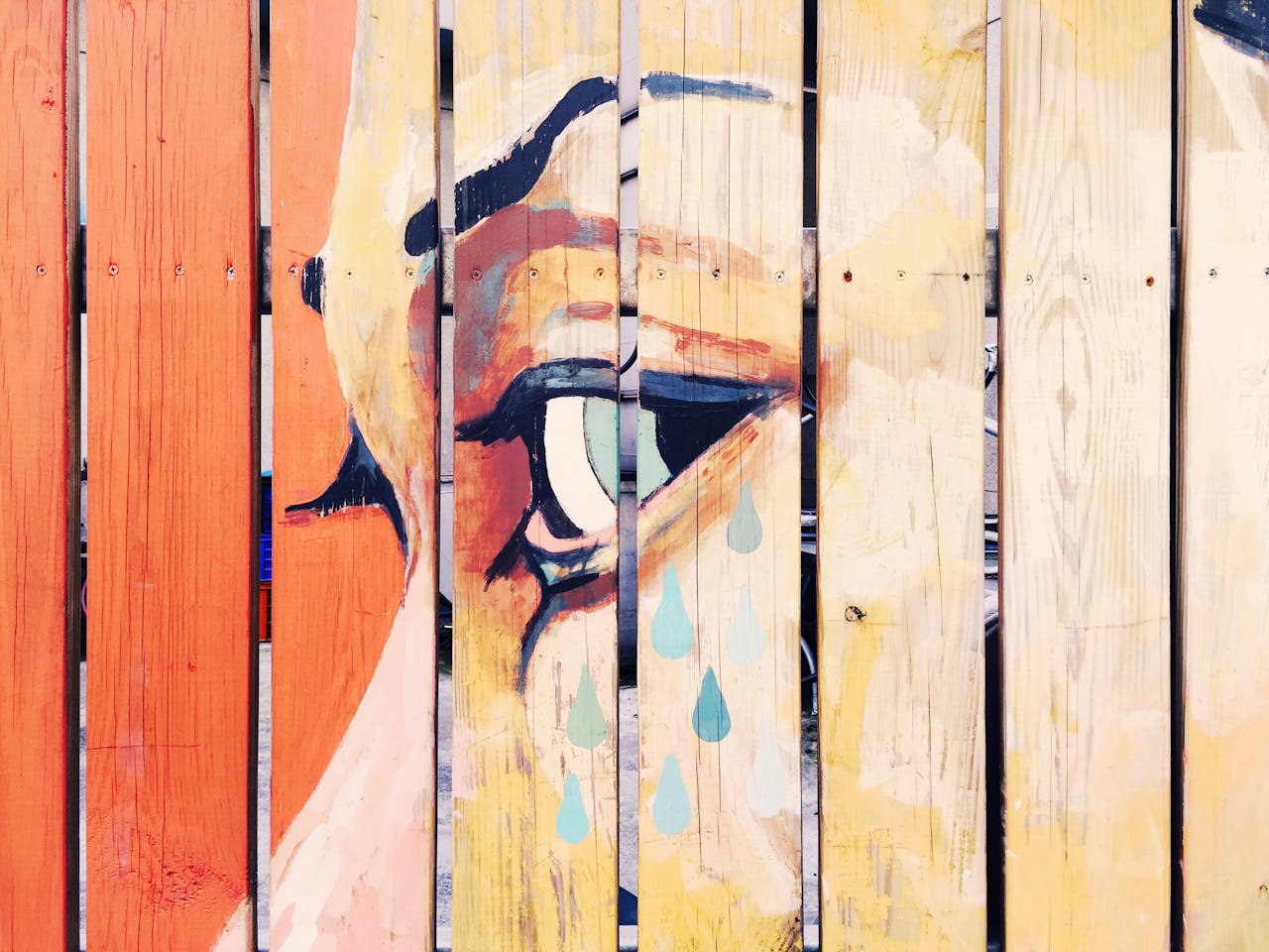 Vivid artistic mural depicting a crying eye painted on a natural wooden fence.